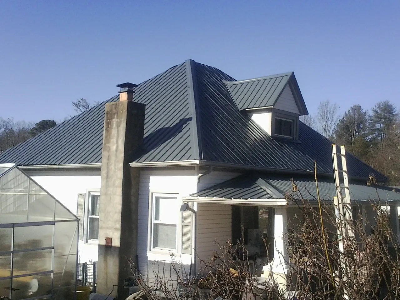 Dark blue standing seam metal roof on a white farmhouse with dormer — Slate & Tile Roof Repair by Roofing Brothers in Riddleton
