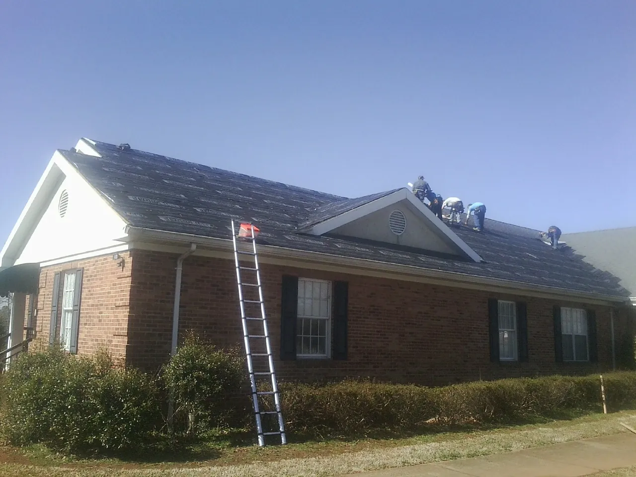 Crew tearing shingles off a brick ranch roof with a ladder set — Metal Roof Repair work by our crew in Riddleton