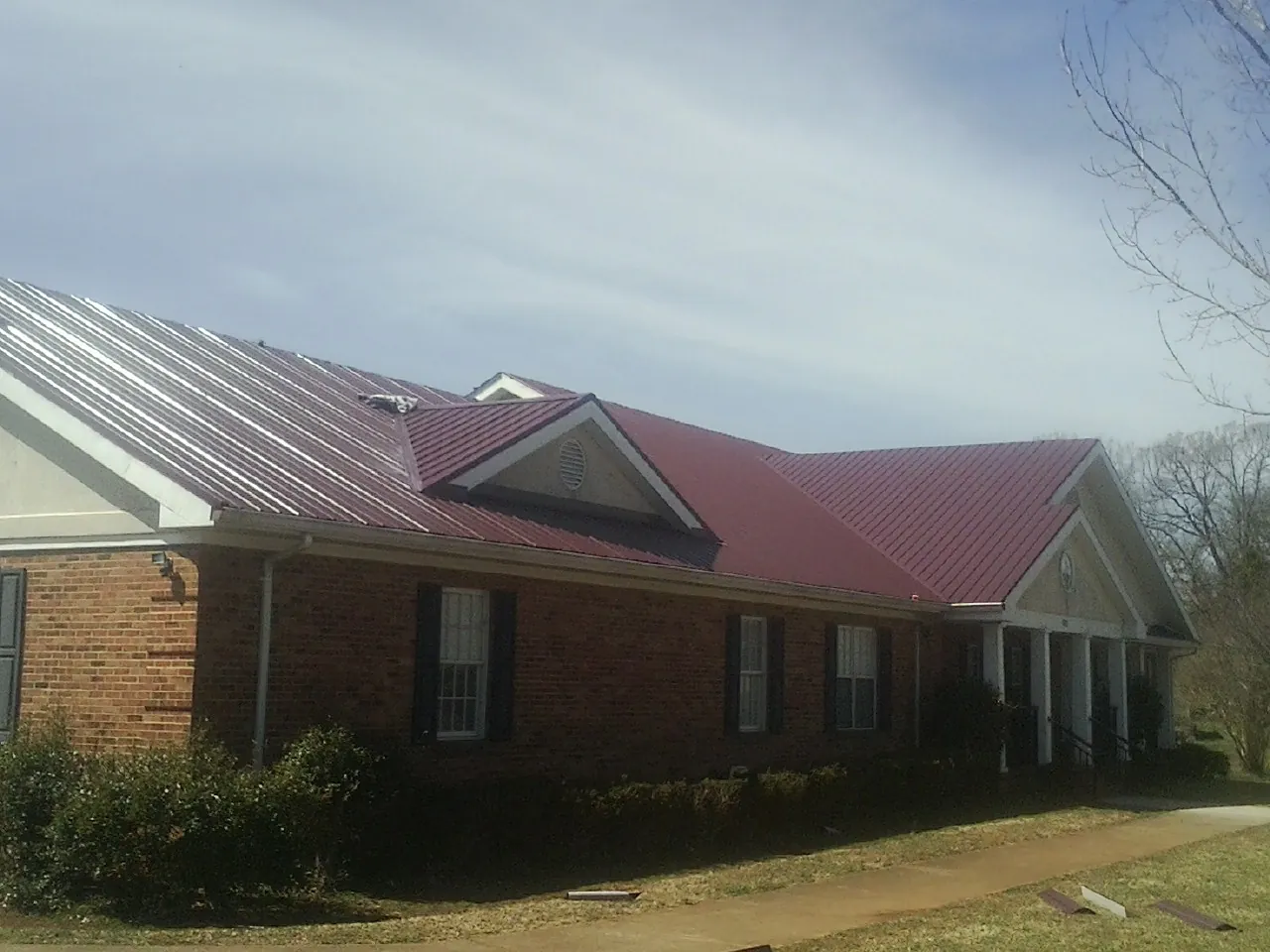 Red metal roof with gabled entries on a long brick building, from a Hail Damage Roof Repair job in Riddleton