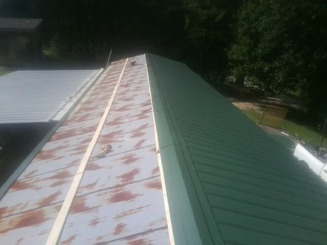 Old rusted panels beside newly installed green metal roofing — Wind Damage Roof Repair by Roofing Brothers in Riddleton
