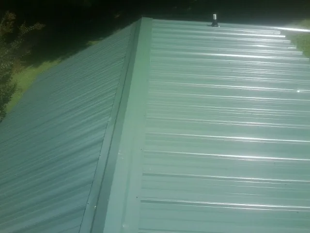 New green metal panels meeting at the ridge of a roof — Flat Roof Repair work by our crew in Riddleton