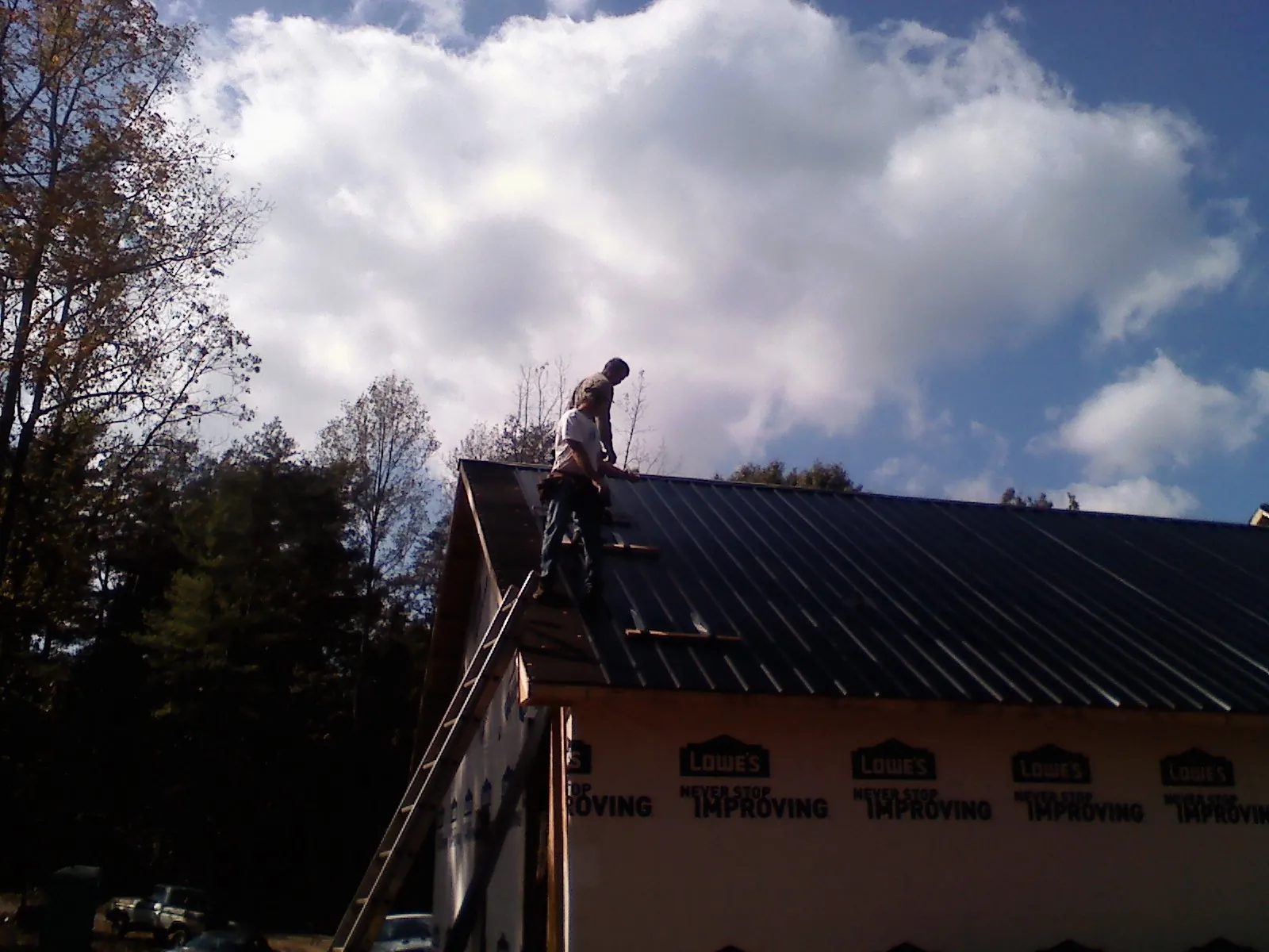 Roofer fastening dark metal panels high against a cloudy sky, from a Roof Inspection job in Riddleton