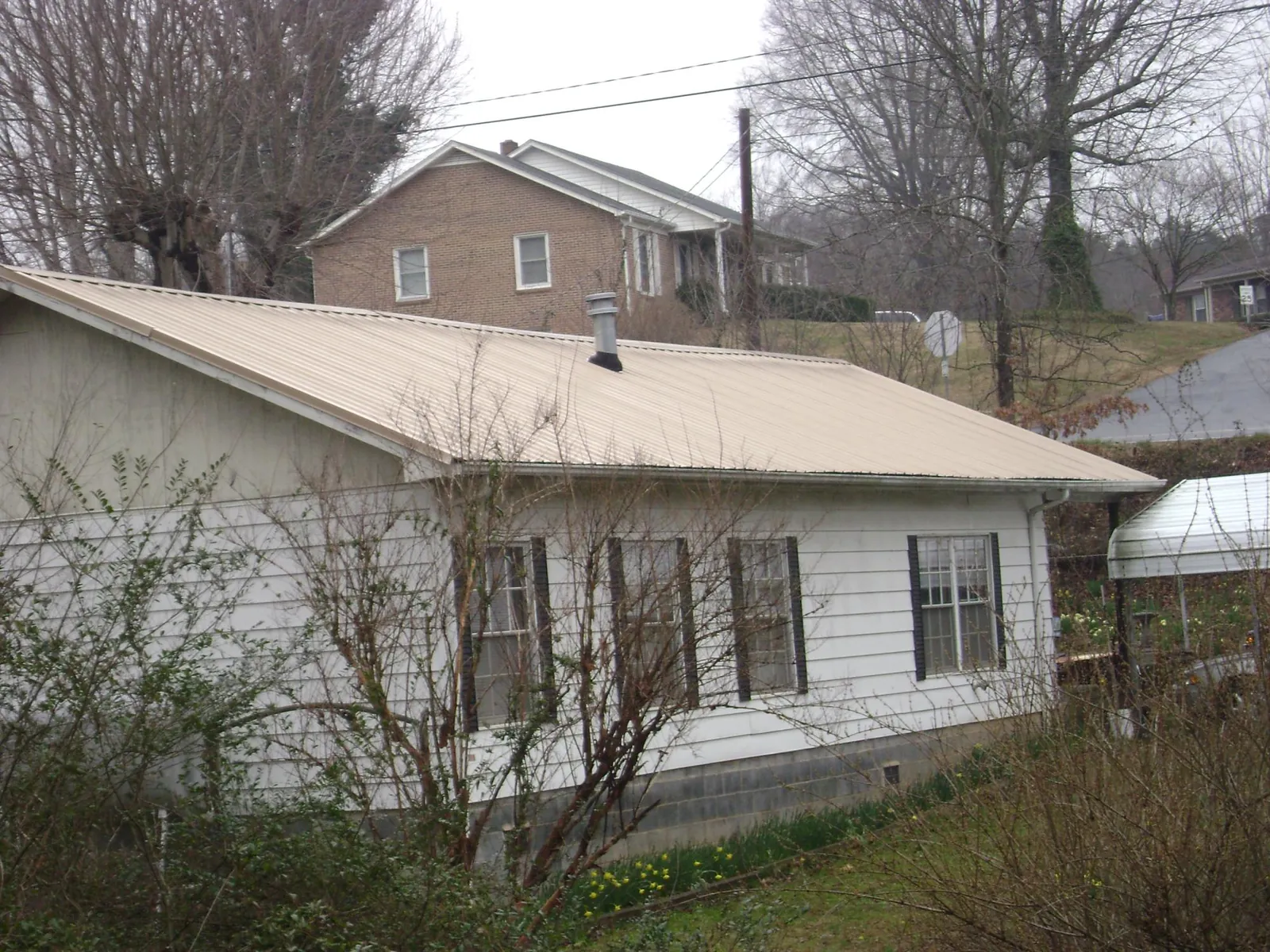 Tan metal roof on a white sided house set into a hillside — Commercial Roofing by Roofing Brothers in Riddleton