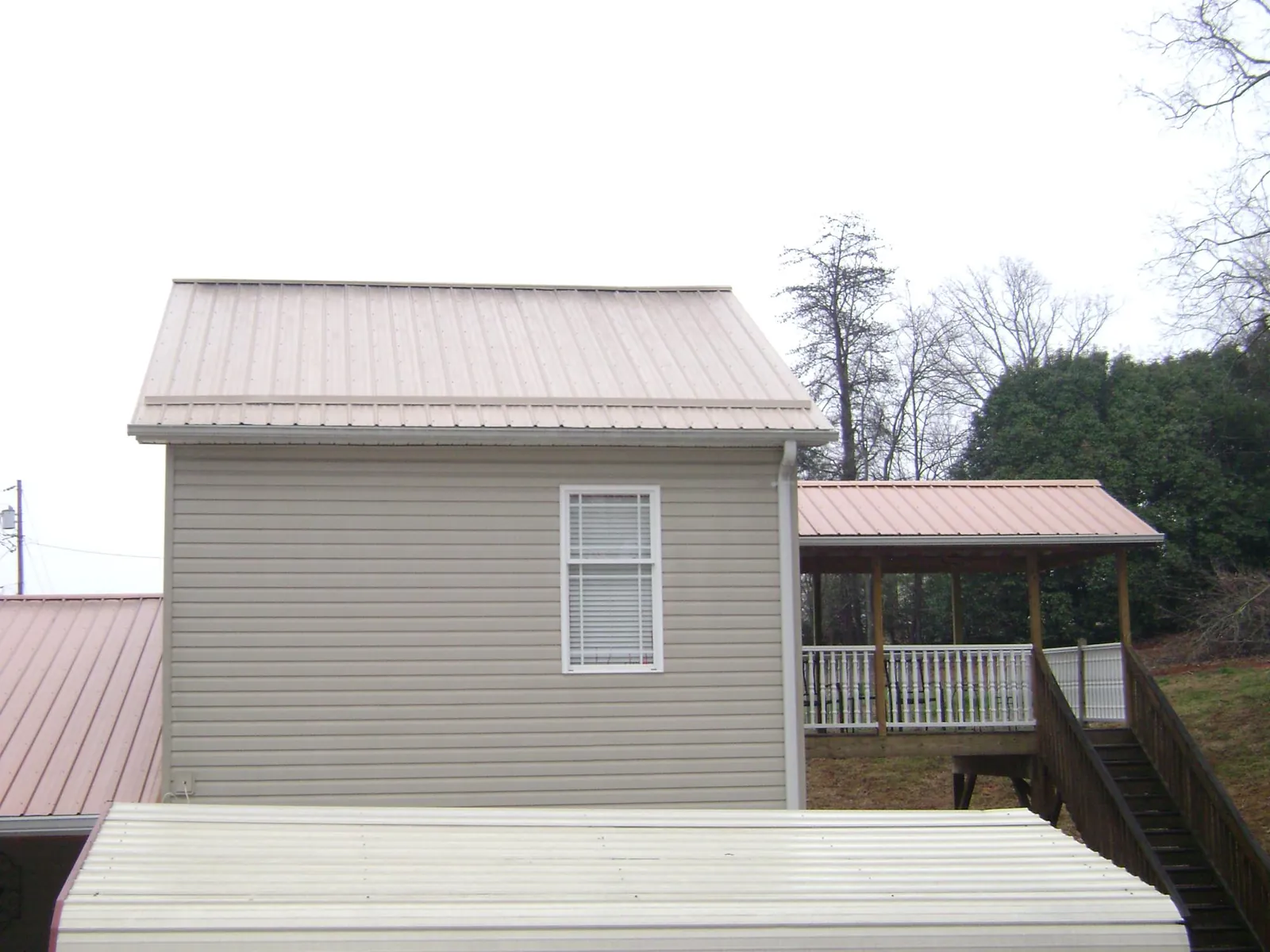 Tan metal roofs on a two story addition and attached porch, from a Roof Replacement job in Riddleton